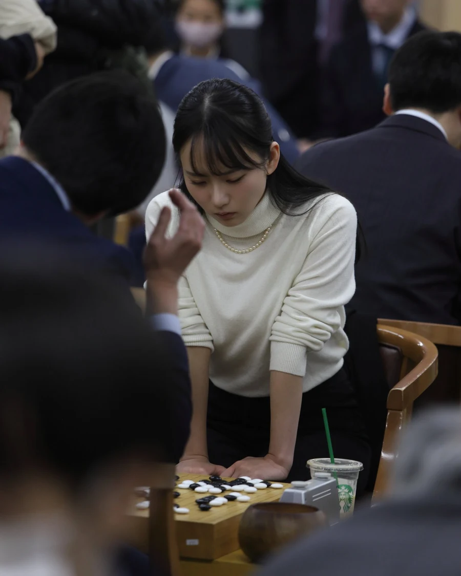 観戦者に囲まれた会場で、碁石を打とうとする三島響と対局相手